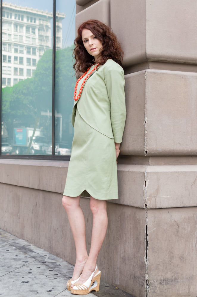 Side view of our Overlapping Front Jacket in Sage Green paired with our Drop Sleeve Scallop Hem Dress in the same color way. Chain long neckless in contrast color, orange, is  a cute idea!